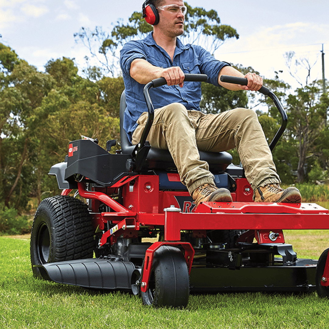 Man operating a red riding lawn mower in an outdoor setting with trees and grass.