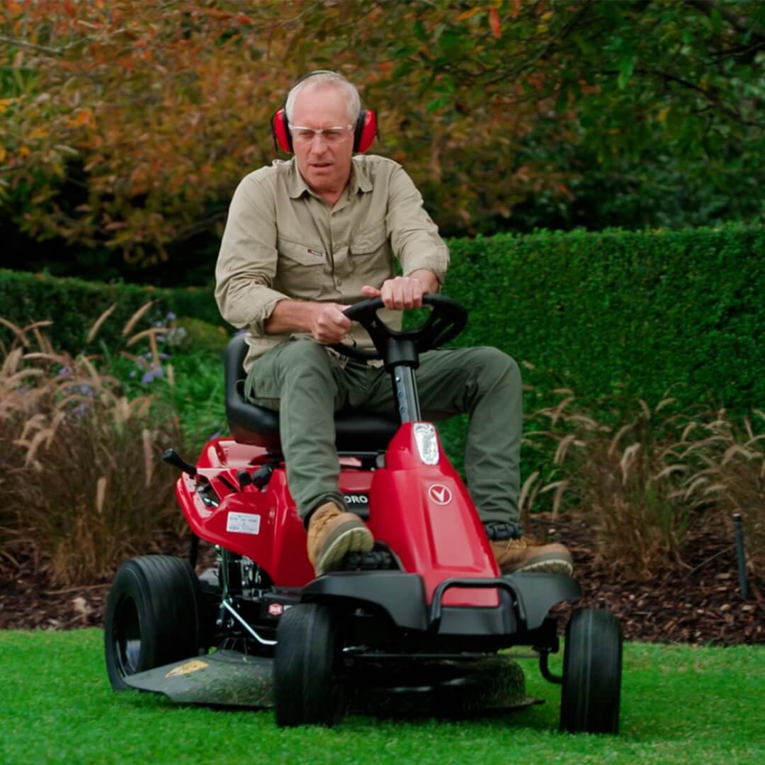 Man operating a red riding lawn mower in a garden setting