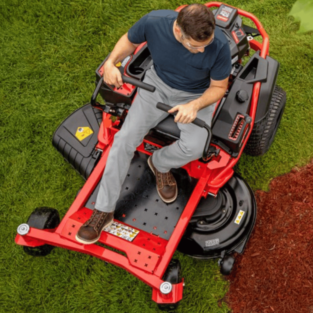 Man operating a red riding lawn mower on grass